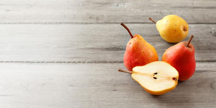 Three whole ripe red and yellow pears, and one cut in half on gray wood boards. Banner size with place for text on the left.