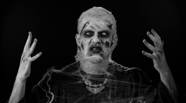 Portrait of sinister man in carnival costume of Halloween crazy zombie with bloody wounded scars face trying to scare isolated on black room. Horror theme of cosplay wounded undead, beast, monster