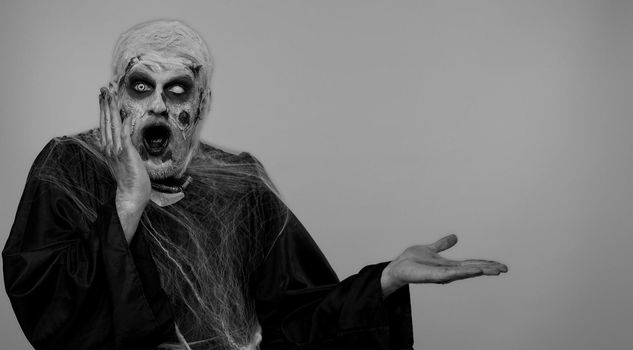 Creepy one man with bloody scars face, Halloween stylish zombie make-up. Scary wounded undead guy showing thumbs up and pointing at left on blank space. Place for your advertisement logo. Chroma key
