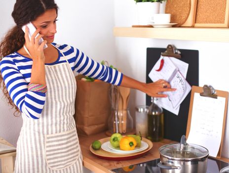 Portrait of a woman text messaging in front of vegetables in the kitchen at home