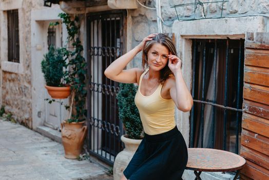 Girl tourist walking through ancient narrow street on a beautiful summer day in MEDITERRANEAN MEDIEVAL CITY , OLD TOWN bUDVA, MONTENEGRO. Young beautiful cheerful woman walking on old street at tropical town. Pretty girl looking at you and smiling