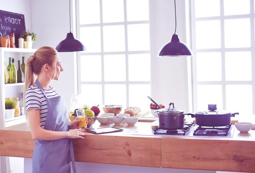 Attractive woman holding a glass of orange juice while standing in the kitchen.