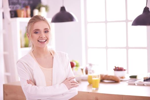 Attractive woman holding a glass of orange juice while standing in the kitchen.