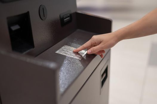 Faceless woman dialing bank card pin at ATM