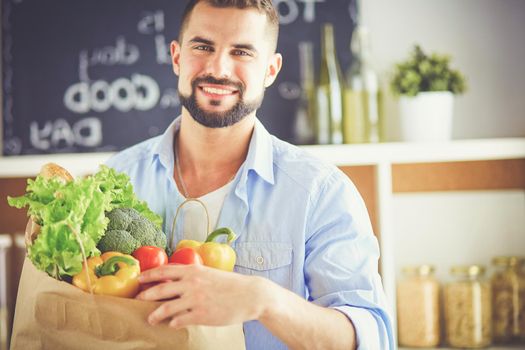 Man holding paper bag full of groceries on the kitchen background. Shopping and healthy food concept.