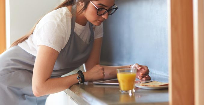 Portrait of young attractive caucasian brunette housewife at kitchen. Morning with cup of coffee and tablet pc.