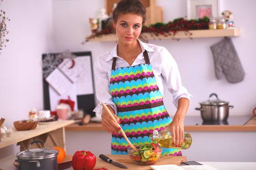 Young woman mixing fresh salad standing near desk .