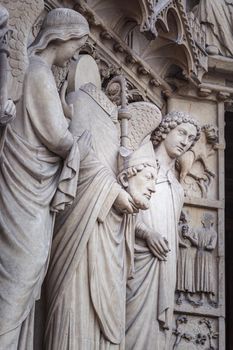 Saint Denis without head and angel, Notre dame facade detail in Paris, France