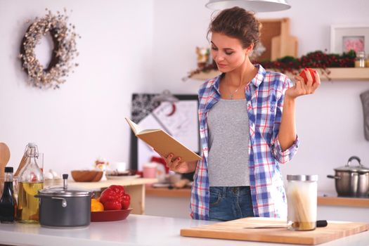 Young woman reading cookbook in the kitchen, looking for recipe, isolated