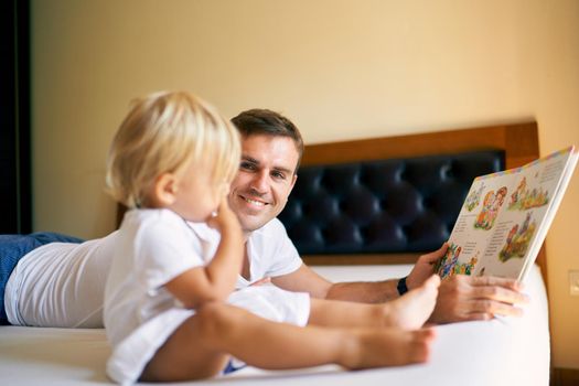 Dad shows a book with bright pictures to a little girl. High quality photo