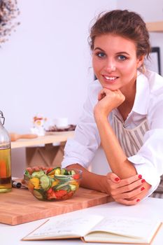 Smiling young woman preparing salad in the kitchen .