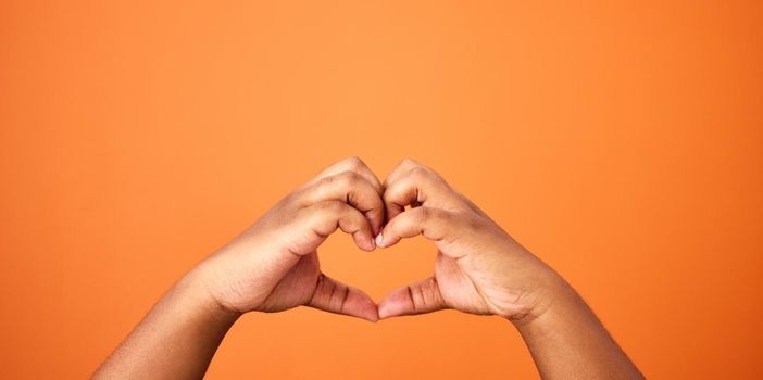 Love is all we need. an unrecognizable person showing a heart gesture against an orange background