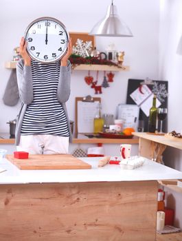 Young woman showing clock in christmas decorated kitchen