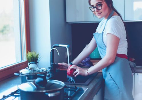 Woman washing vegetables. Beautiful young woman washing vegetables for salad and smiling while standing in the kitchen.