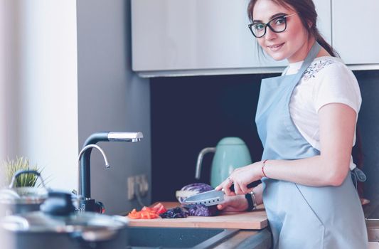 Young woman cutting vegetables in kitchen standing near desk.