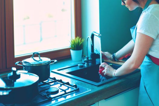 Woman washing vegetables. Beautiful young woman washing vegetables for salad and smiling while standing in the kitchen.