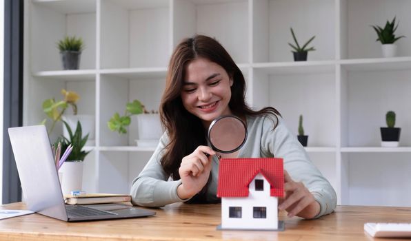 Happy woman hand holding magnifying glass and looking at house model, house selection, real estate concept..