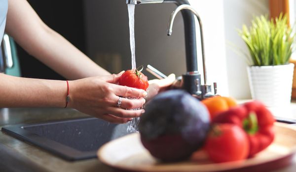 Woman washing tomatoes in kitchen sink close up.