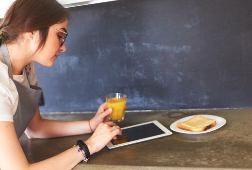 Portrait of young attractive caucasian brunette housewife at kitchen. Morning with cup of coffee and tablet pc.