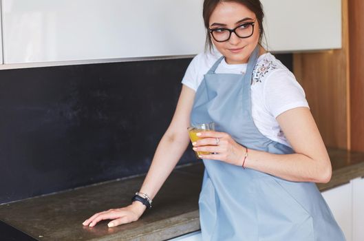 Attractive woman holding a glass of orange juice while standing in the kitchen.