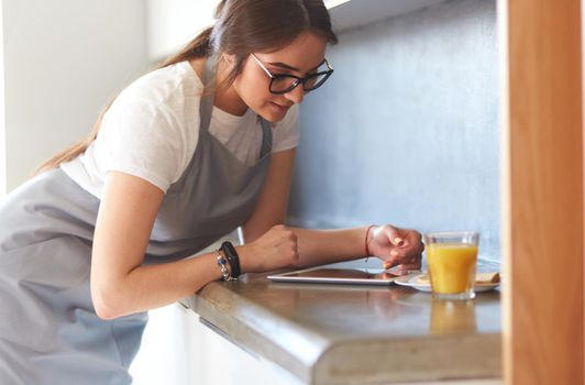 Young woman with orange juice and tablet in kitchen.