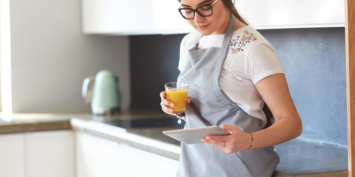 Young woman with orange juice and tablet in kitchen.