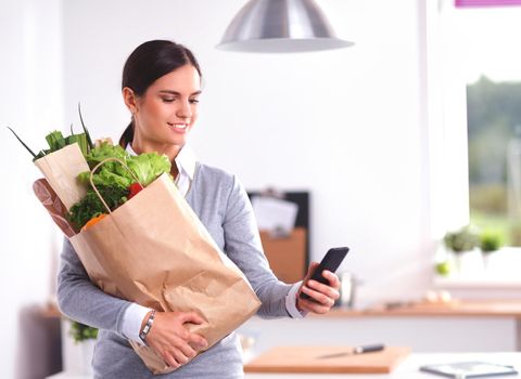 Young woman holding grocery shopping bag with vegetables .Standing in the kitchen.