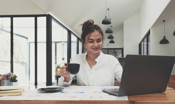 Smiling Asian businesswoman holding a coffee mug and laptop at the office.