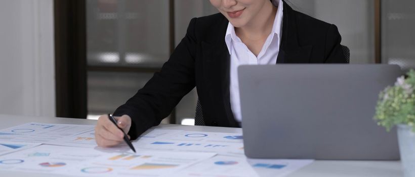 Beautiful smiling Asian businesswoman working pointing on a graph at the office.