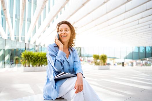 Attractive brunette businesswoman talking mobile phone with client. Pretty caucasian female business person smile when phone conversation. Woman managing business talking via mobile phone sitting