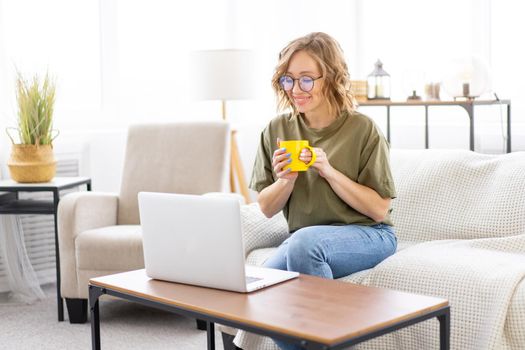Woman with glasses use laptop typing keyboard sitting couch big window background home interior Freelance female working from home Distance learning student relaxing watch lessons video conference.