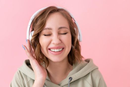 Happy teeth smile woman listen music headphones Caucasian female enjoy podcast or audio books dressed oversize hoodie pink background close up portrait