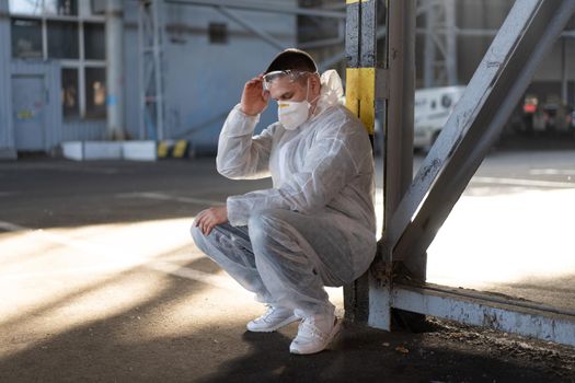 Despair healthcare worker in white covid protective overalls.Tired Male caucasian doctor grabs his head cower in depression during coronavirus pandemic Paramedic overworked cry covered face with hands