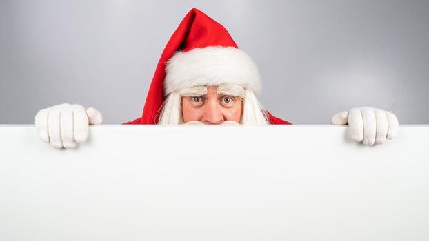 Santa Claus peeks out from behind an ad on a white background. Merry Christmas