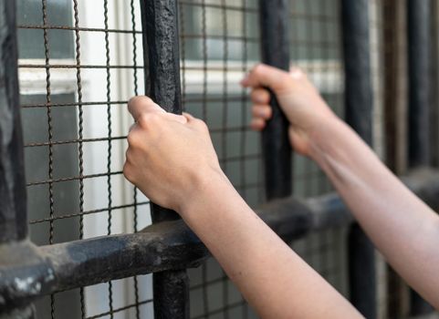 Woman in prison hands of behind hold Steel cage jail bars. offender criminal locked in jail. Prisoner hands close up holding metal cage in jail. law concept