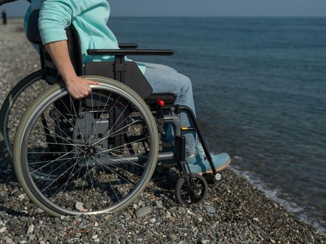 Caucasian woman in a wheelchair on the seashore. Close-up of female hands