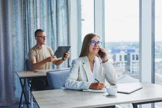 Portrait of a female manager in formal attire doing office work and talking on the phone, a successful european female boss in optical glasses for vision correction, posing at her desk