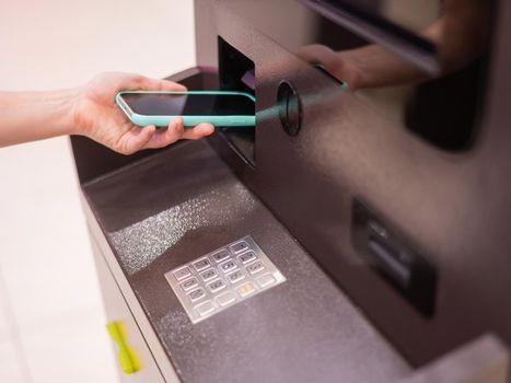 Woman using smartphone online financial transactions at ATM. NFC online banking concept