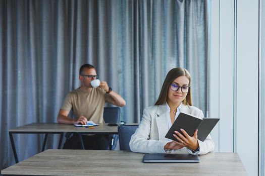 A business woman is holding a notepad and using a laptop while her European colleague is working in the background. Concept of modern successful women. Office workers sitting at desks in the office