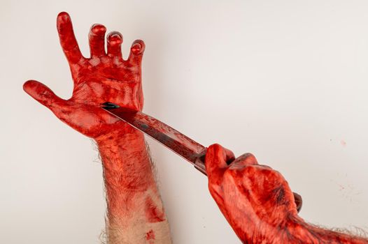 A man with bloody hands cuts himself with a knife