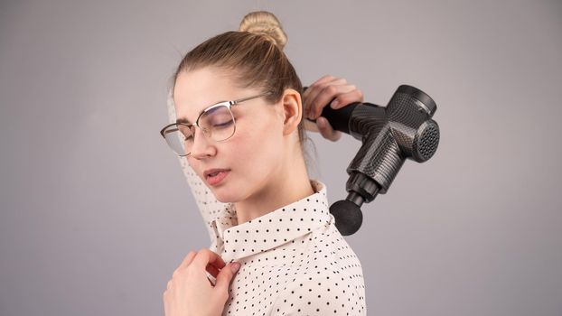 Caucasian business lady makes herself a back massage with a massager gun on a white background