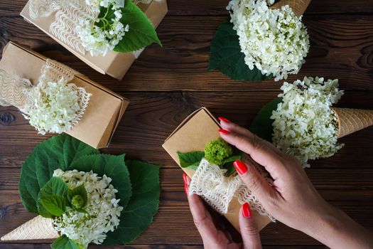 Women's hands pack a gift in a craft box with hydrangea flowers. High quality photo