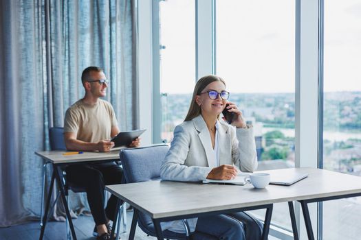 Portrait of a female manager in formal attire doing office work and talking on the phone, a successful european female boss in optical glasses for vision correction, posing at her desk