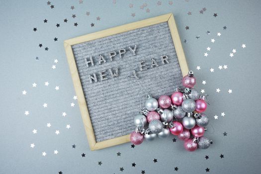 The happy new year inscription is laid out on a gray background decorated with silver stars and Christmas balls. High quality photo