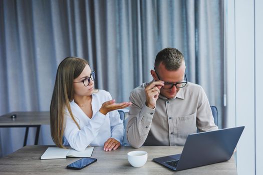 Businessmen are discussing while working with laptop in the office. Focused business people cooperating in a modern workspace. Two young businessmen are sitting together at a table.