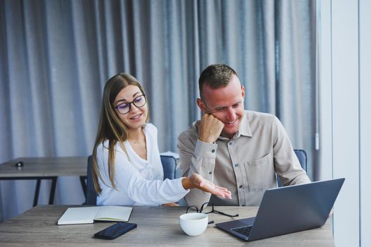 Businessmen are discussing while working with laptop in the office. Focused business people cooperating in a modern workspace. Two young businessmen are sitting together at a table.