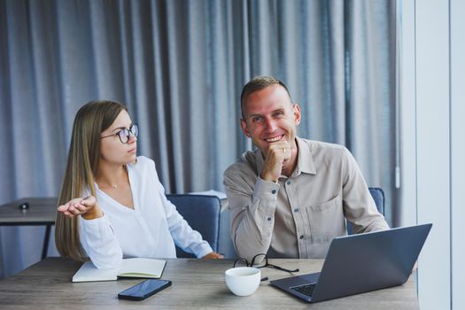 Businessmen are discussing while working with laptop in the office. Focused business people cooperating in a modern workspace. Two young businessmen are sitting together at a table.