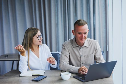 Businessmen are discussing while working with laptop in the office. Focused business people cooperating in a modern workspace. Two young businessmen are sitting together at a table.