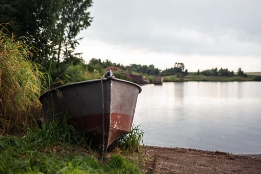 A motor boat is parked at the shore of a lake or river in the evening at sunset or early in the morning. The boat is in a quiet place next to the reeds and is ready for fishing.