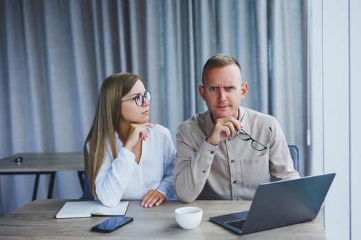 Businessmen are discussing while working with laptop in the office. Focused business people cooperating in a modern workspace. Two young businessmen are sitting together at a table.